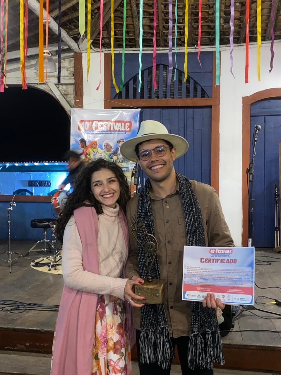 Mariana e Vinícius segurando o troféu e o certificado do Festival da Canção, em julho de 2025