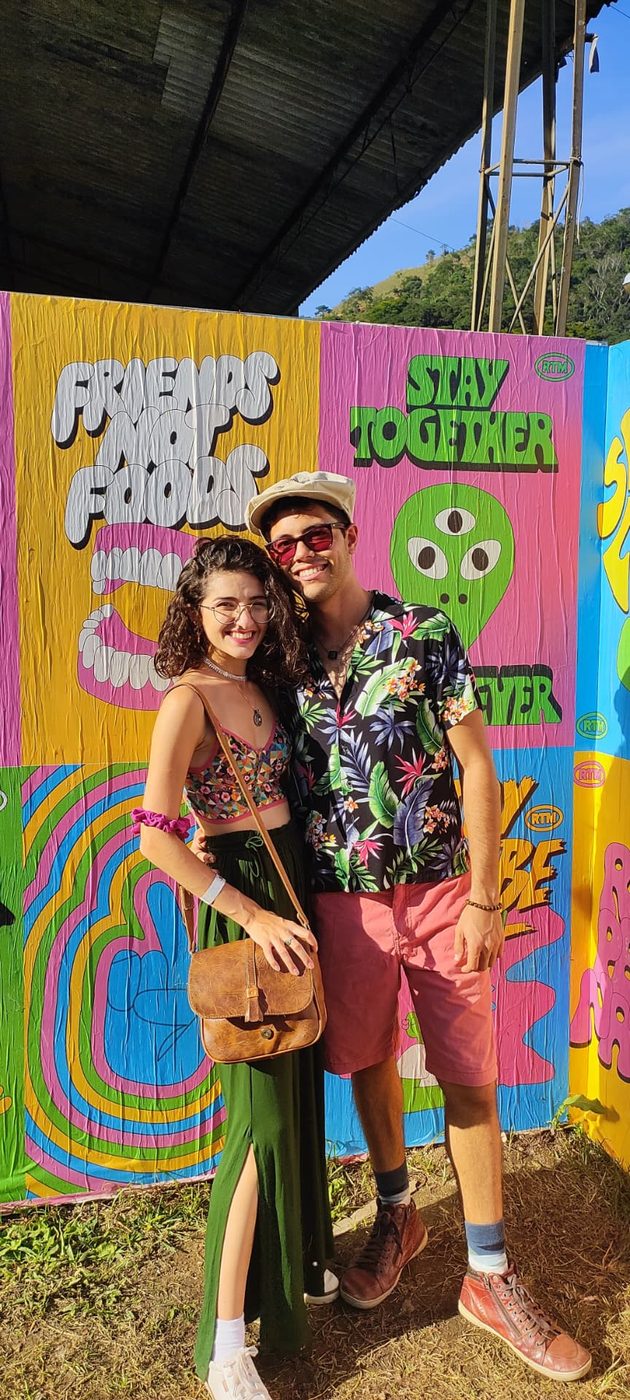 Mariana e Vinícius em frente a um painel colorido no primeiro festival de música que foram juntos, em 2022
